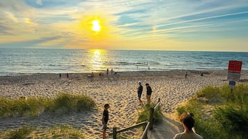 Een strand met een houten looppad dat naar het water leidt, een heldere lucht en de zon die onder de horizon verdwijnt.