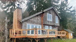 A two-story wooden house with a deck, surrounded by trees. - Charming beachfront 1-bedroom cottage near Langley, Whidbey Island Washington. (Langley)