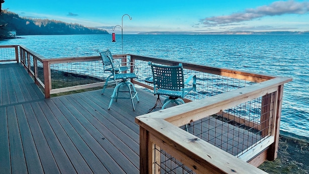 A wooden deck with metal railings overlooking a body of water. - Charming beachfront 1-bedroom cottage near Langley, Whidbey Island Washington. (Langley)