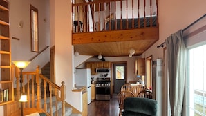 A spacious living area with a staircase leading to a loft, a dining area, and a kitchen with modern appliances. - Charming beachfront 1-bedroom cottage near Langley, Whidbey Island Washington. (Langley)