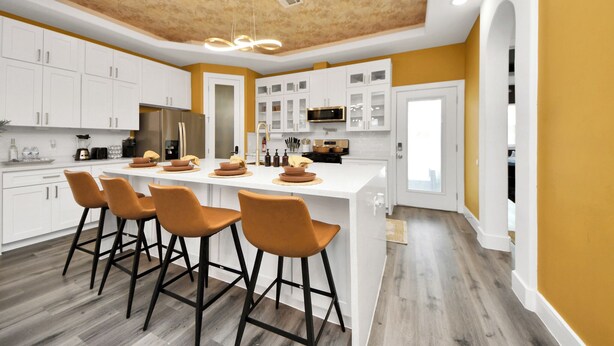 Una cocina moderna con armarios blancos, una isla central con taburetes altos y un techo de madera.