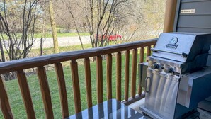 Una parrilla Cuisinart sobre una terraza de madera, con vistas a un jardín césped y un coche rojo al fondo.