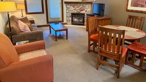 Una sala de estar con chimenea, televisor y comedor con sillas de madera y una mesa.