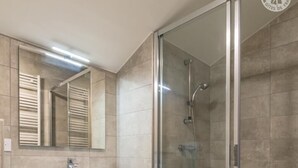 A bathroom with a wooden vanity, a glass shower enclosure, and a tiled floor.
