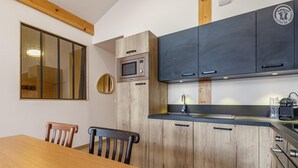 A compact kitchen with wooden cabinets, a microwave, a sink, and a dining table with chairs.