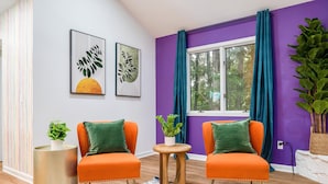 Une pièce avec deux fauteuils orange, une petite table ronde en bois et une fenêtre ornée de rideaux violets.