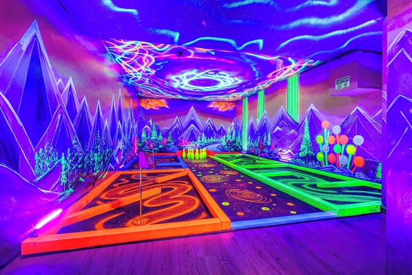 A neon-lit indoor space with geometric patterns on the floor and walls, and a caution sign on the wall. - OMG! Indoor Mini Golf, Bowling, Theater, Hot Tub (McGaheysville)