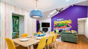 Un coin repas avec une table en bois, des chaises jaunes et un mur violet orné d’une pancarte de bienvenue.