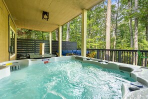 A hot tub on a covered deck with a view of a forest. - OMG! Indoor Mini Golf, Bowling, Theater, Hot Tub (McGaheysville)