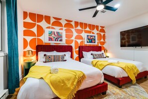 A hotel room with two beds, each with red headboards, white bedding, and yellow throw blankets. The walls have a geometric orange and white pattern. - OMG! Indoor Mini Golf, Bowling, Theater, Hot Tub (McGaheysville)