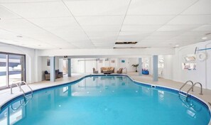 An indoor swimming pool with clear blue water, surrounded by a white interior, and a seating area with chairs and a sofa.