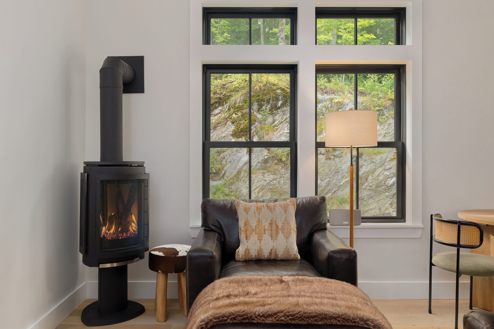 Ein gemütlicher Raum mit Kaminofen, einer Ledersofa, einem kleinen Holzschemel und einem Tisch mit Lampe.
