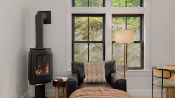 Ein gemütlicher Raum mit Kaminofen, einer Ledersofa, einem kleinen Holzschemel und einem Tisch mit Lampe.