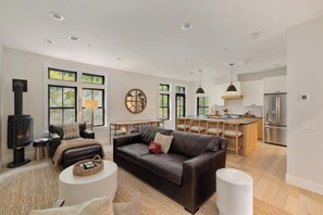 A modern living room with a fireplace, leather sofa, and a dining area with a kitchen in the background.