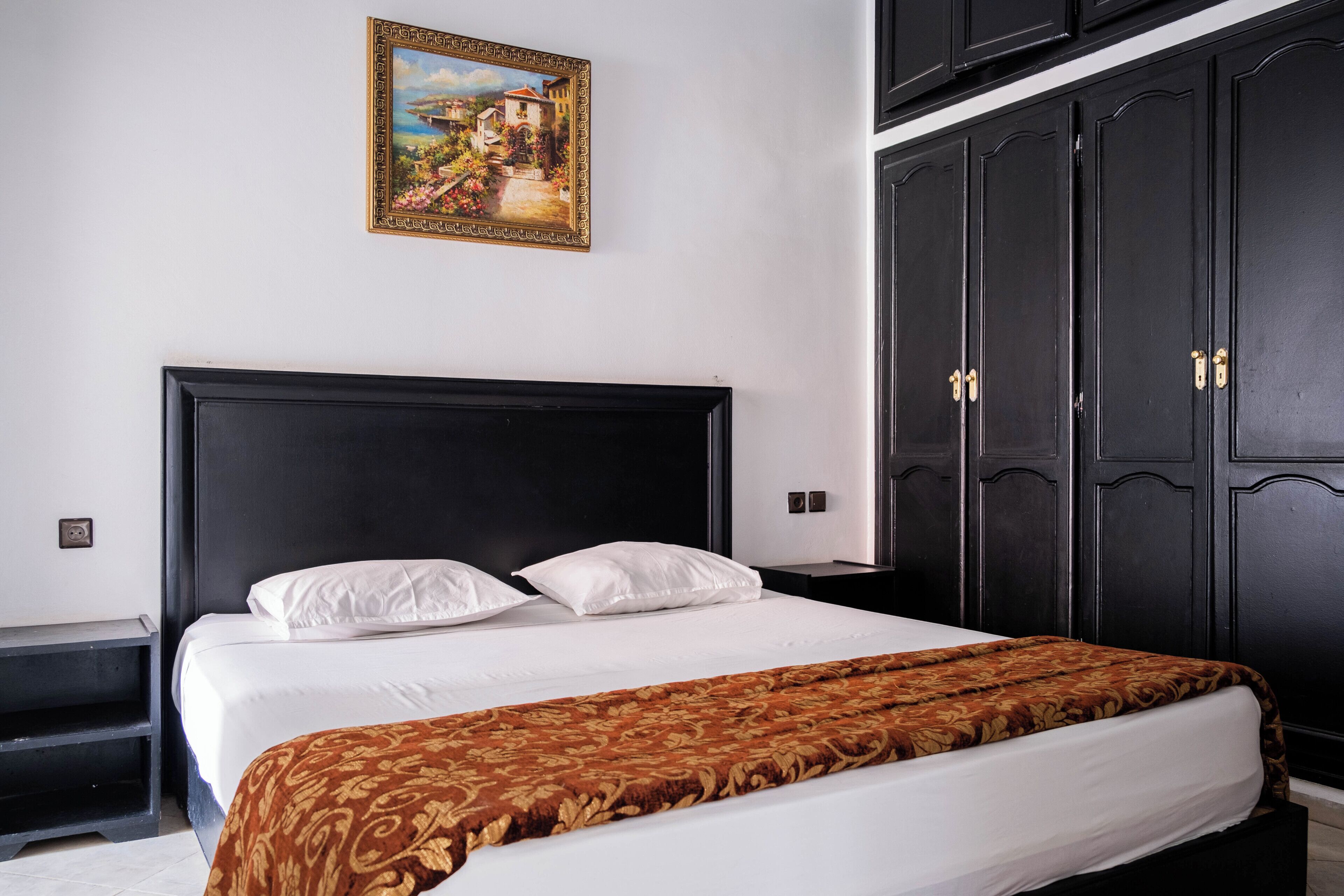 A bedroom with a large bed, a dark wooden wardrobe, and a framed picture on the wall.
