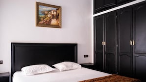 A hotel room with a large bed, a nightstand, a wardrobe, and a framed painting on the wall. - Hotel Appart Larabi (Marrakech)