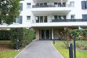 A modern two-story building with a covered entrance, a balcony with a railing, and a pathway leading to the entrance.