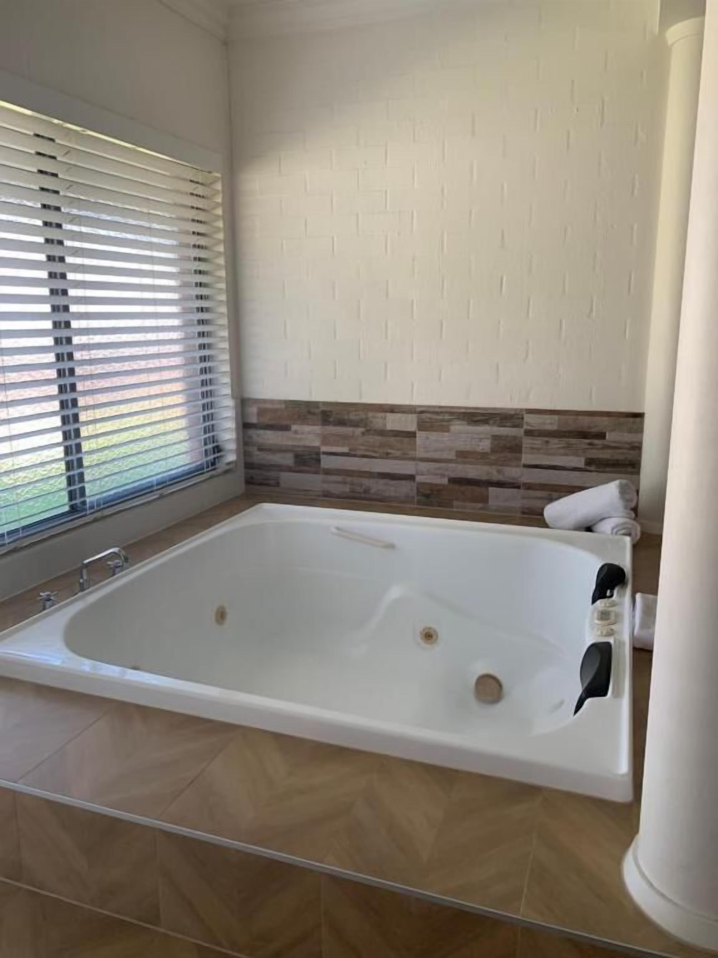 Uma casa de banho moderna com uma banheira grande, uma janela com persianas e uma parede revestida a azulejos.