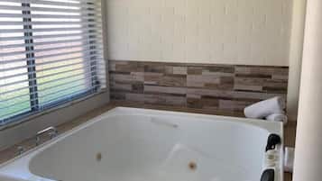Uma casa de banho moderna com uma banheira grande, uma janela com persianas e uma parede revestida a azulejos.