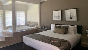 Ein Hotelzimmer mit einem großen Bett, einer Sitzecke mit Blick auf den Pool, einer Badewanne und zwei gerahmten Bildern an der Wand.