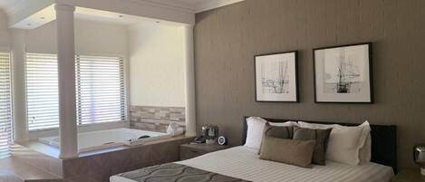 Habitación de hotel con una cama grande, una zona de estar con vistas a la piscina, una bañera y dos cuadros en la pared.