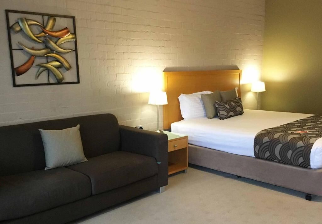 A hotel room with a bed, a nightstand, a sofa, and a wall-mounted artwork.