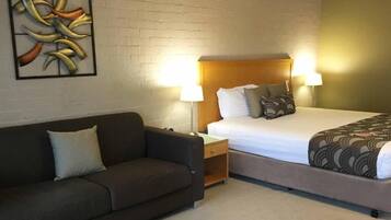 A hotel room with a bed, a nightstand, a sofa, and a wall-mounted artwork.