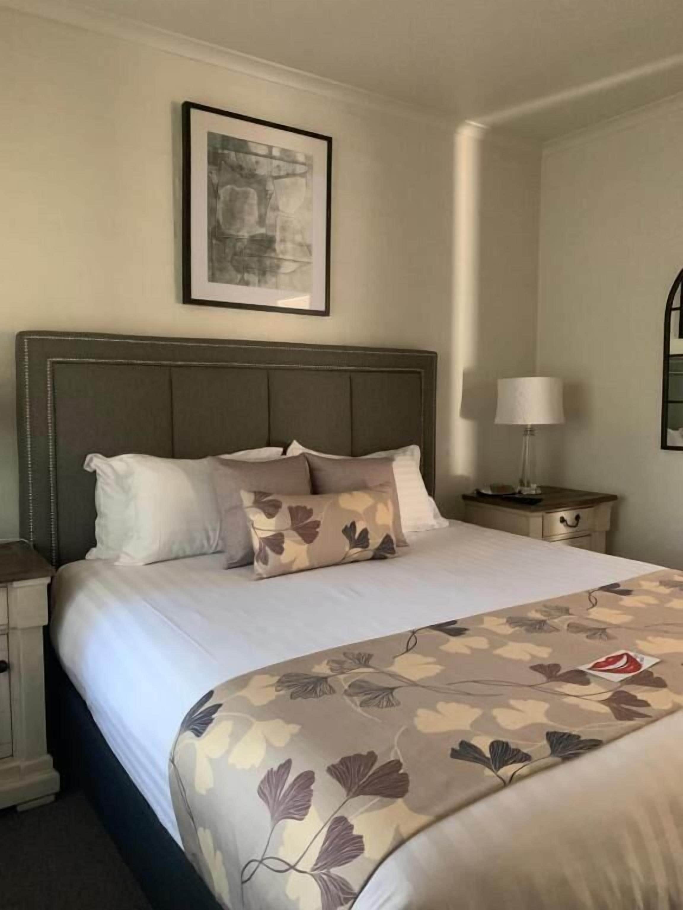 Una cama bien hecha con cubrecama estampado con motivos florales, un cabecero y un cuadro enmarcado en la pared.