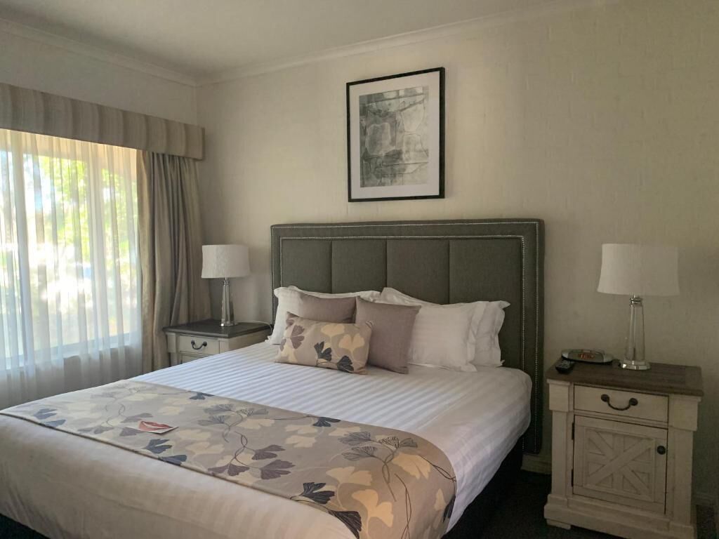 A hotel room with a large bed, two bedside tables with lamps, a framed picture on the wall, and a window with curtains.
