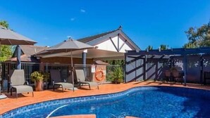 Ein Pool mit Whirlpool, umgeben von Liegestühlen und Sonnenschirmen, im Hintergrund eine überdachte Terrasse.