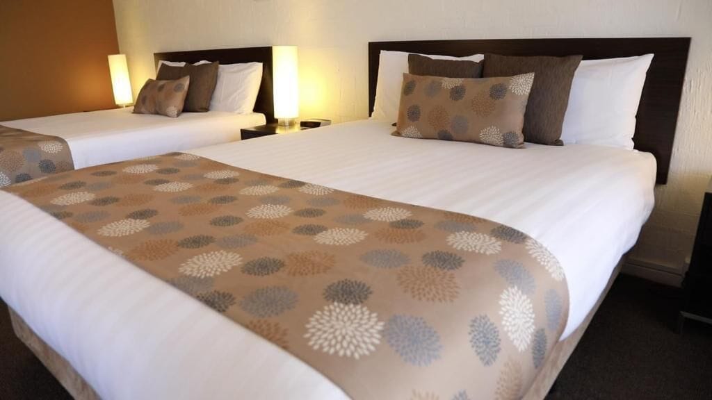 A hotel room with two beds, each with a headboard, bedside tables, and lamps.