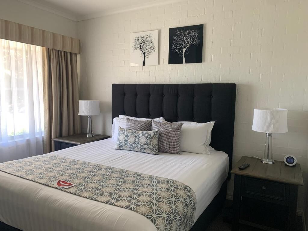 Habitación de hotel con una cama grande, dos mesitas de noche y dos lámparas de pared.