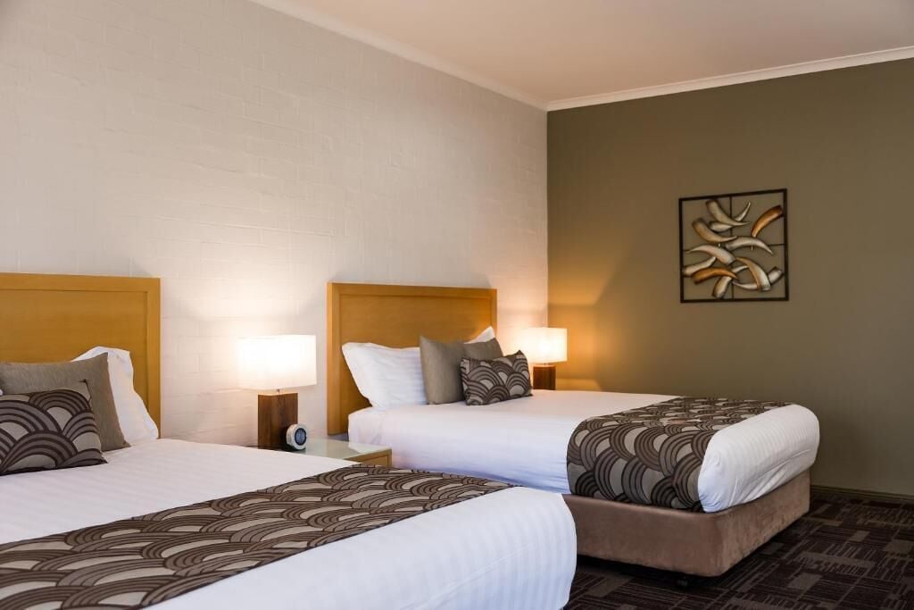A hotel room with two beds, each with a headboard, bedside tables, and lamps.
