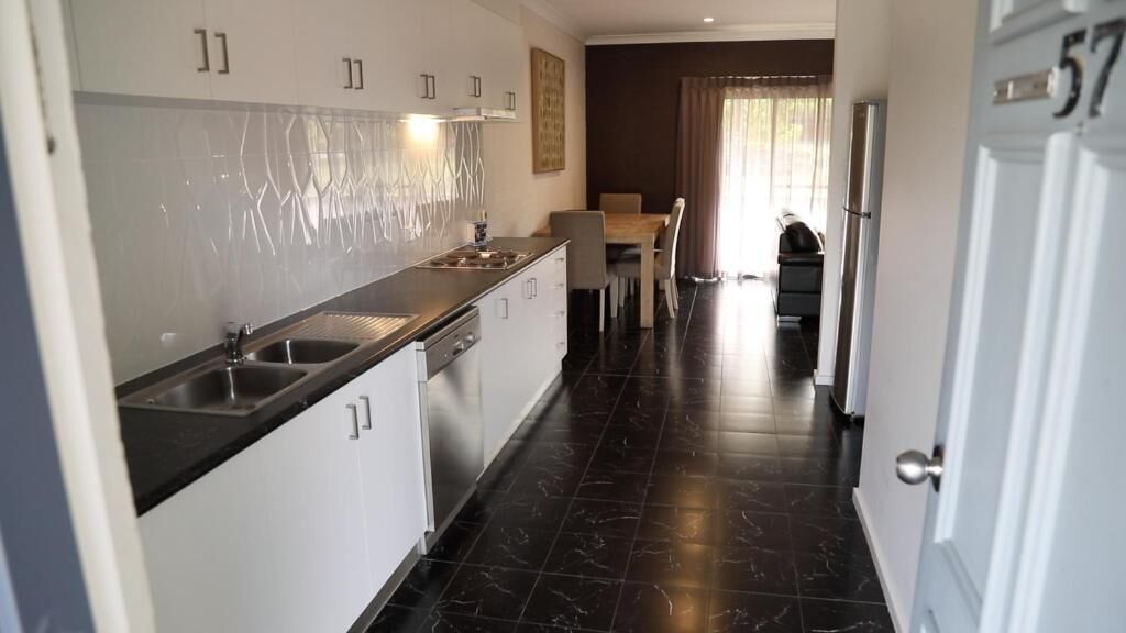 A modern kitchen with white cabinets, black countertops, and a black tiled floor. There is a dining area with a table and chairs in the background.