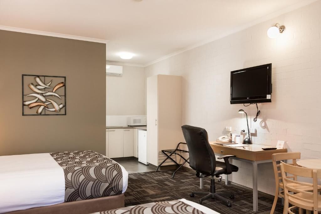 A hotel room with a bed, a desk with a chair, a television, and a microwave in the background.