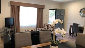 Ein modernes Wohnzimmer mit Esstisch, Stühlen, einem Fernseher und einer Topforchidee.