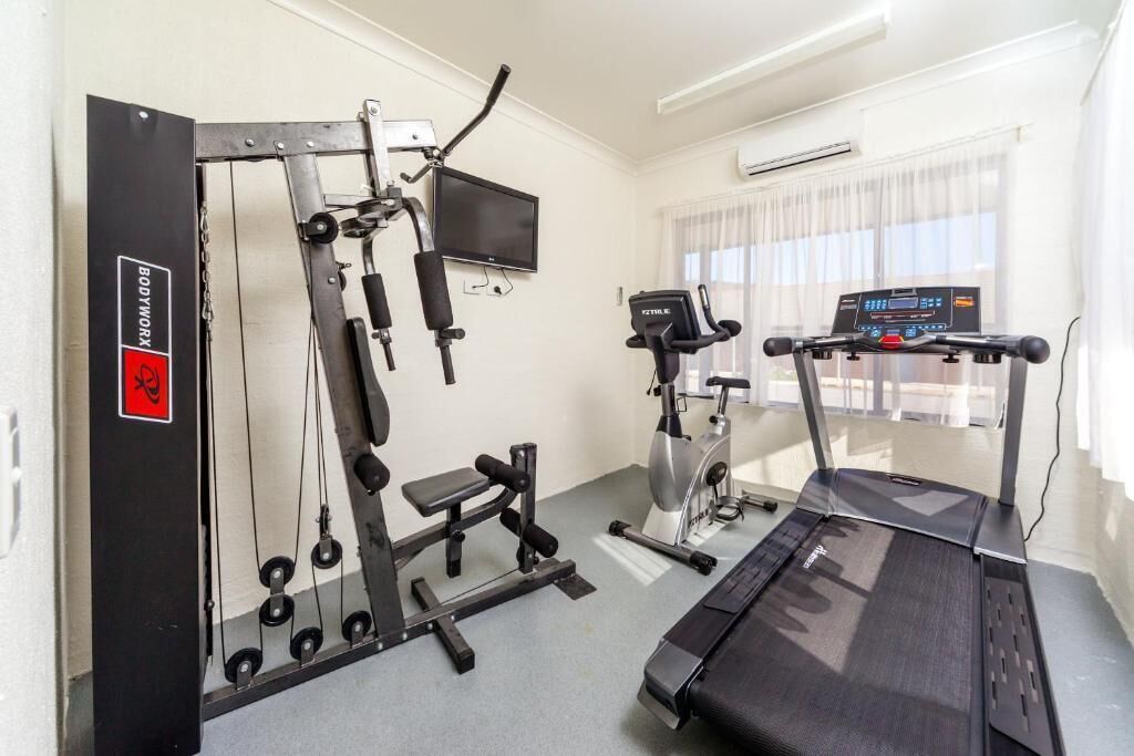 Une salle de sport équipée de machines de cardio, d’un banc de musculation et d’un tapis de course.