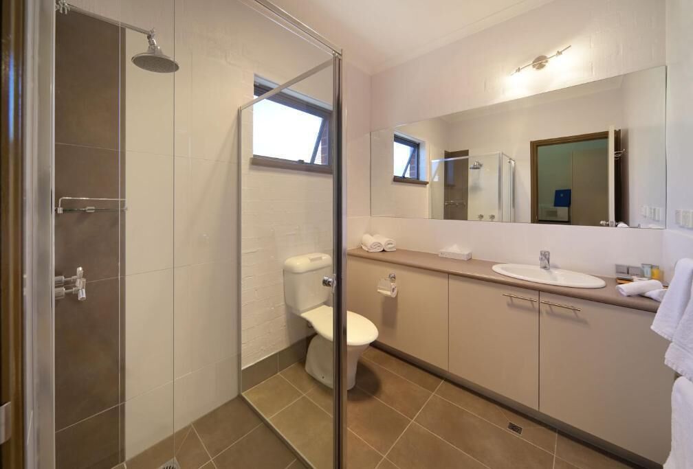 Ein modernes Badezimmer mit Duschkabine aus Glas, Toilette, Waschbecken und Spiegel.