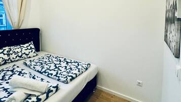 Un dormitorio con cama, cabecero, ventana con cortinas, piso de madera e imagen colgada en la pared.