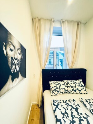 Een slaapkamer met een bed, een raam met gordijnen en een kunstwerk aan de muur.