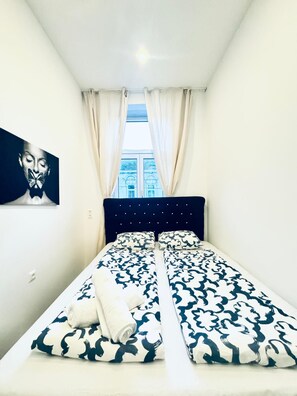 Une chambre à coucher avec un lit, des rideaux, un tableau et une fenêtre donnant sur des immeubles.