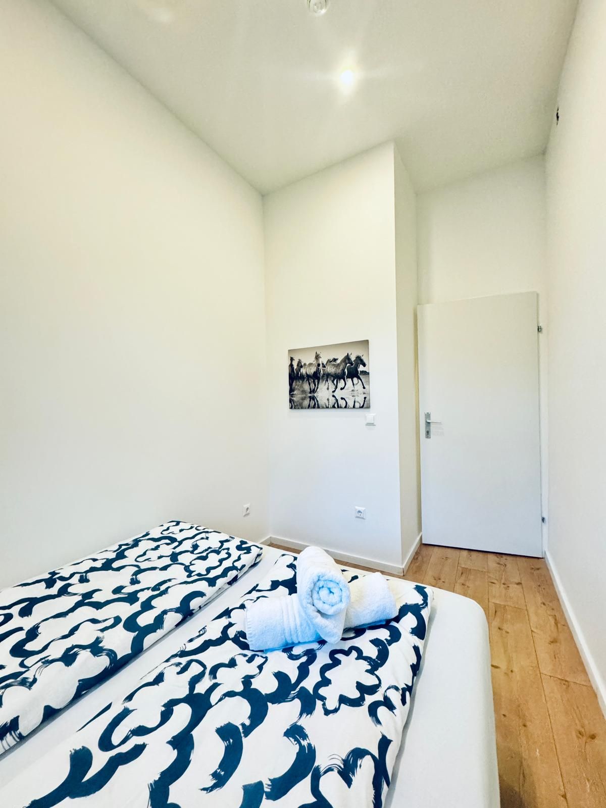 Un dormitorio con cama, una puerta blanca y un cuadro colgado en la pared.