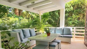 Un patio al aire libre con mobiliario de mimbre, una mesa de vidrio y plantas en macetas.