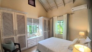 Un dormitorio con cama, mesita de noche, silla, armario y ventana con cortinas.