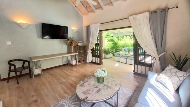 Una sala de estar con ventilador de techo, televisor montado en la pared, sofá, mesa de centro y vista a un patio exterior.