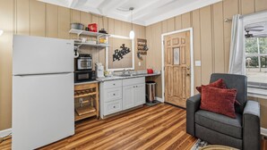 A compact kitchen with a refrigerator, microwave, and coffee maker. There is a wooden door and a window with curtains.
