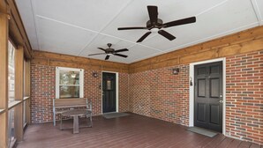 A covered porch with a brick wall, a wooden bench, a table, and two ceiling fans.
