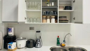 A kitchen with white cabinets, a sink, a blender, a rice cooker, and various kitchen utensils.