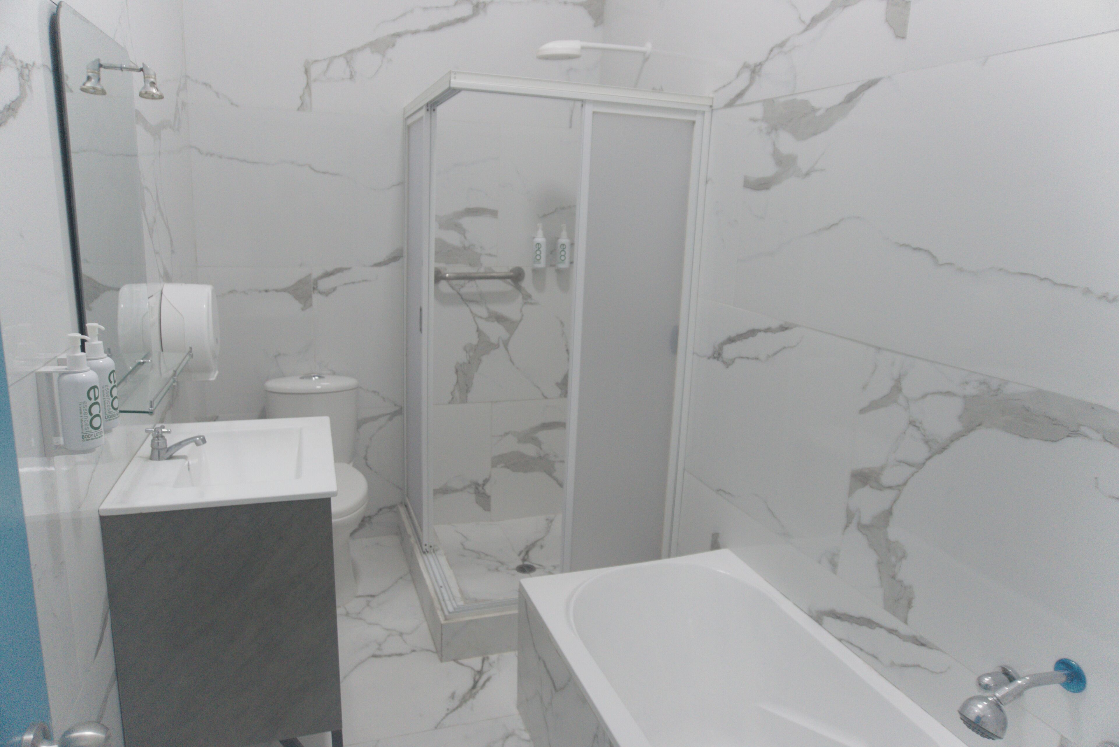 Un baño con suelo de mármol, lavamanos blanco, bañera y cabina de ducha.