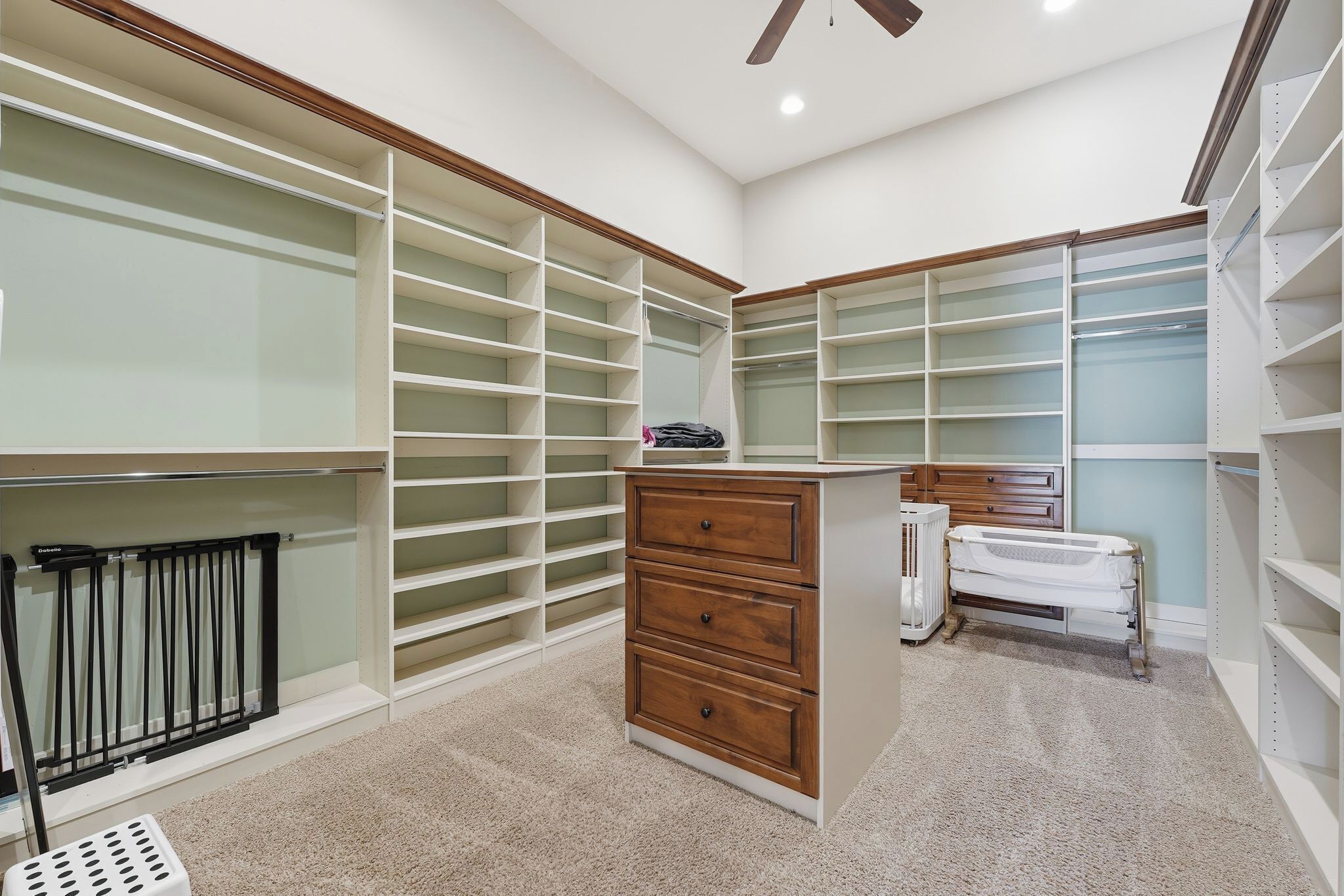 A walk-in closet with multiple shelves, a wooden dresser, and a crib.